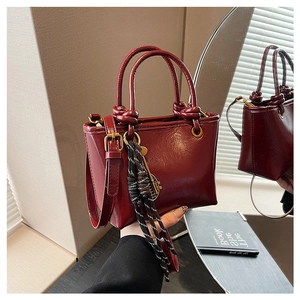 Détail du sac seau bordeaux en cuir verni avec poignées nouées et breloque tissée