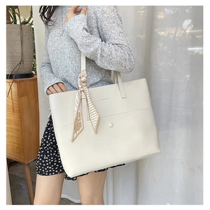 Close-up of white lychee leather tote bag with decorative scarf on the handle strap