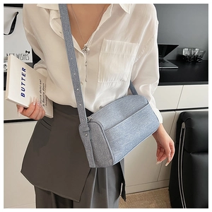 Close-up of a blue denim crossbody bag with adjustable strap worn by a model in casual style