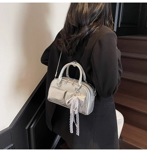 Close-up of silver Boston bag with lace bow charm worn by a model on stairs