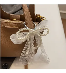 Close-up of elegant pearl lace bow charm attached to a brown leather bucket bag