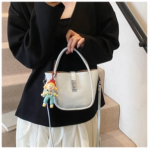 Close-up of white patent leather bucket bag with silver buckle and cartoon doll charm