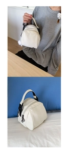 Detail view of white nylon shell bag showing double zippers and plush ball charm accessory