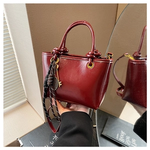 Détail d'un sac seau rouge foncé au fini brillant avec des breloques clés dorées