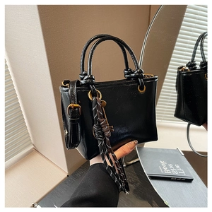 Mini sac seau noir brillant avec charme tissé et poignée nouée vu dans le miroir