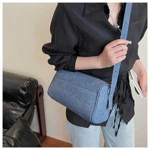 Close-up of a stylish blue denim cylinder crossbody bag worn by a model in a modern room