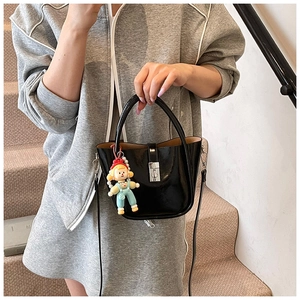 Detail of black patent leather bucket bag with silver clasp and cute cartoon doll charm