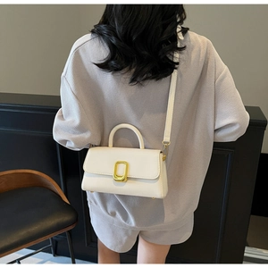 Petit sac à main carré blanc crème porté à l'épaule par un mannequin au style minimal