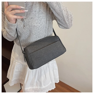 Detail of dark grey denim crossbody bag with zipper and slim strap on shoulder