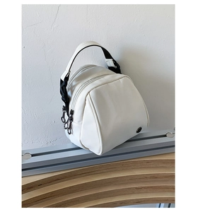 Detail of white minimalist shell crossbody bag featuring black straps and metal logo