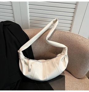 Close-up of beige ruched crescent bag with natural leather texture on a minimal sofa