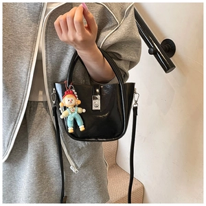 Detail of a black glossy bucket bag featuring silver twist lock and cartoon character charm