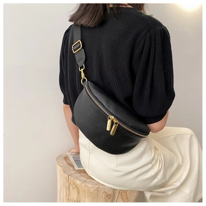 Detail of black pebbled leather crossbody bag with gold zippers and adjustable strap