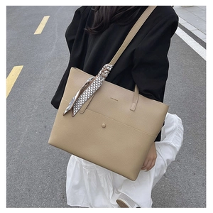 Detail of beige pebbled leather tote bag with silk scarf on handle in street style setting