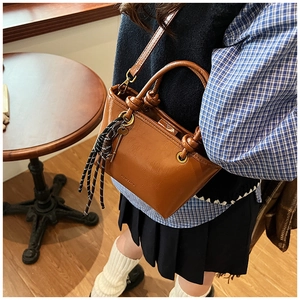 Détail du sac seau en cuir marron avec poignée nouée, anneaux en métal et breloque