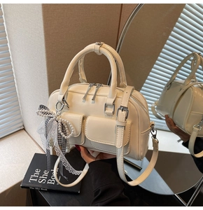 Detail of off-white Boston bag with front pockets and pearl bow charm accessory