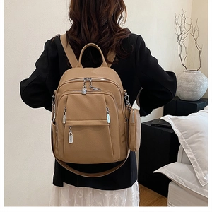 Detailed view of khaki leather backpack with multiple zippers and side pouch on model