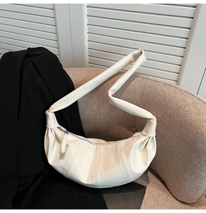 Detailed texture of white crescent bag on a brown sofa with a black blazer accent