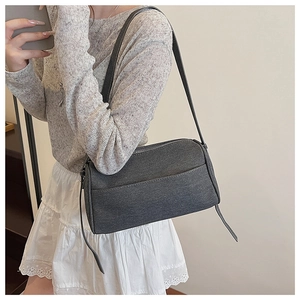 Detail view of grey denim crossbody bag featuring textured fabric and metal zipper closure