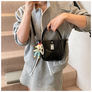 Detail view of a black glossy bucket bag with a silver square lock and pearl chain accessory