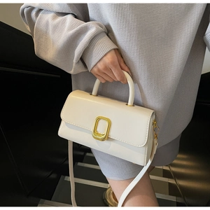Petit sac carré crème chic avec boucle dorée porté à l'épaule dans un cadre moderne