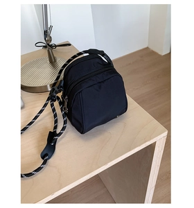 Detail of black nylon shell bag featuring multi-pocket design and striped rope shoulder strap