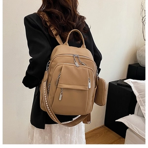 Detail view of khaki pebbled leather backpack with woven strap and small round coin purse charm