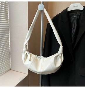 Detailed view of a white crescent shoulder bag in glossy leather on a metal display stand
