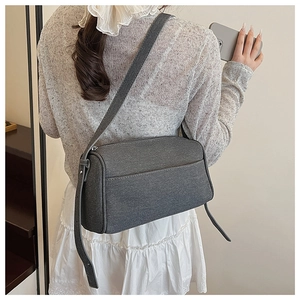 Detail view of the gray textured crossbody bag back pocket and adjustable strap on a model