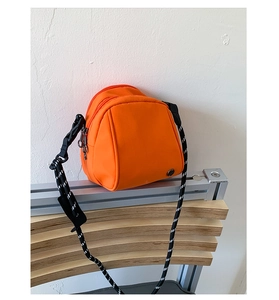 Detail of bright orange crossbody bag with double zippers and rope strap on wooden bench