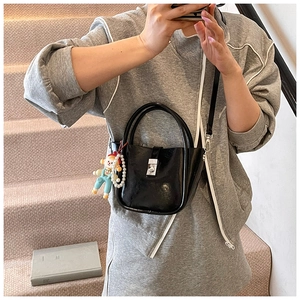 Detail of a shiny black bucket bag featuring a metal twist lock and a pearl doll charm