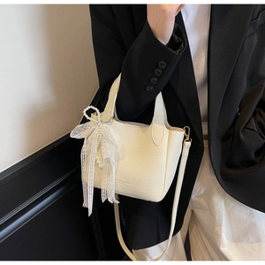 Close-up of white lychee leather bucket bag with pearl lace bow charm and gold hardware