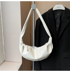 Macro shot of white pleated crescent bag featuring glossy leather and knot strap detail