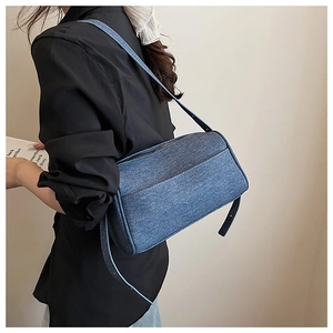 Detailed close-up of blue denim texture and front slip pocket on minimalist shoulder bag