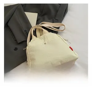 Detail of cream canvas chest bag with silver snap button and red decorative side label