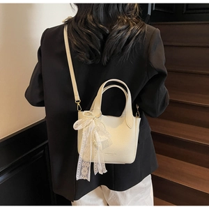 Detail of cream bucket bag with lychee texture leather, lace bow, and pearl charms