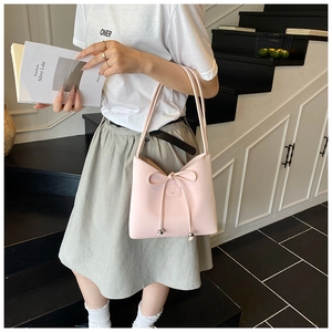 Détail du sac cabas en cuir rose avec nœud décoratif porté à l'épaule par un mannequin