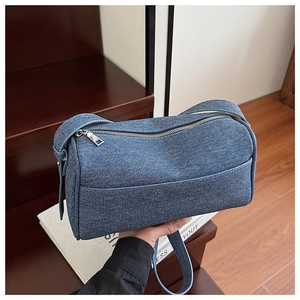 Detail of blue denim shoulder bag with silver zipper and adjustable strap on wood stairs