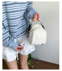 Detail of a minimalist off-white crossbody shell bag with a cute cat plush pendant charm