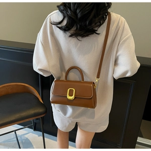 Petit sac carré marron avec fermoir doré porté par un modèle pour montrer la taille
