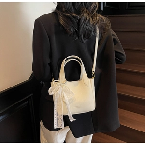 Close-up of off-white lychee leather bucket bag with lace and pearl bow charm detail