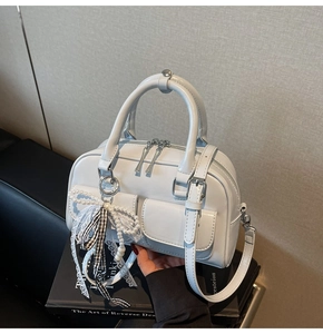 Detail view of white Boston bag with pearl lace charm and dual front pockets