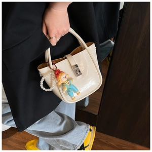 Detail of cream patent leather bucket bag with silver lock and cute cartoon doll charm
