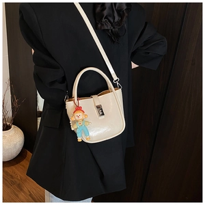 Close-up of minimalist cream leather bucket bag with silver buckle and cute doll pendant