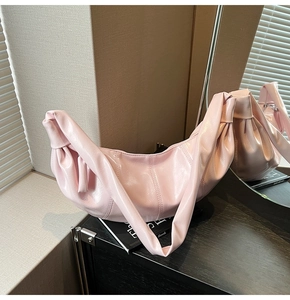 Detail of light pink crescent bag with glossy leather texture and pleated handle design