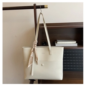 Detail of creamy white pebble leather tote bag with silk scarf on a wooden hanger
