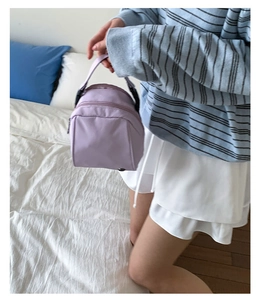 Detail view of a compact lavender nylon shell bag with sturdy woven handle and zipper close