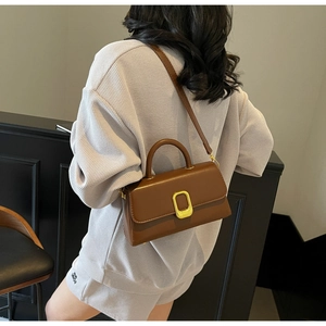 Détail d'un sac à bandoulière marron avec boucle dorée porté par un mannequin