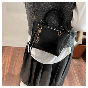 Détail d'un sac seau noir brillant avec logo HIMEIHU et pendentif nœud rayé
