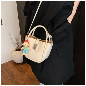 Detail of cream-white bucket bag with silver twist lock and colorful charm accessory